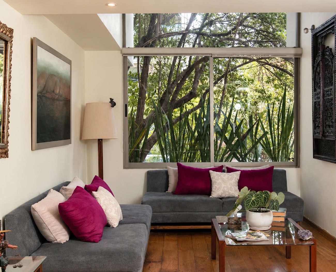 La sala de espera: dos sofás grises con cojines color vino, una ventana amplia hacia la vegetación y una mesa de centro con libros.